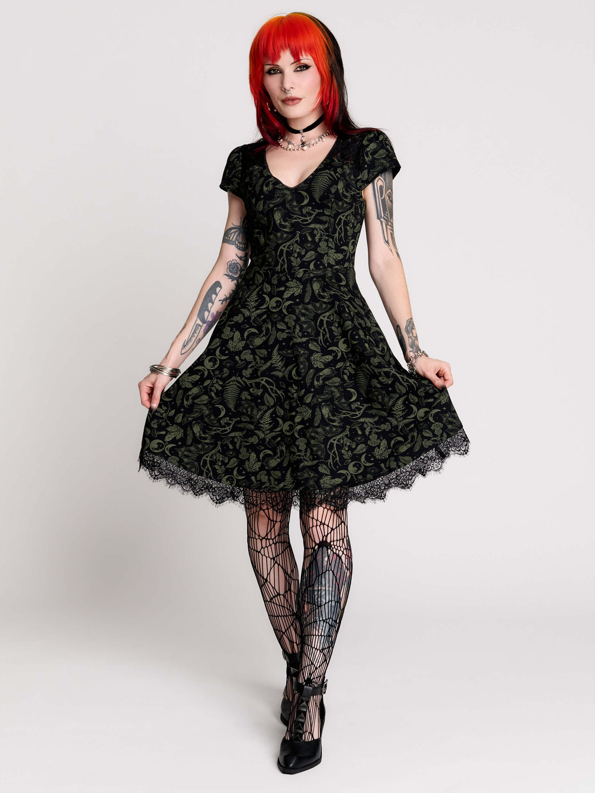 short black dress with a green leafy lace pattern, featuring cap sleeves, a V-neckline, side pockets, and a scalloped lace hem.