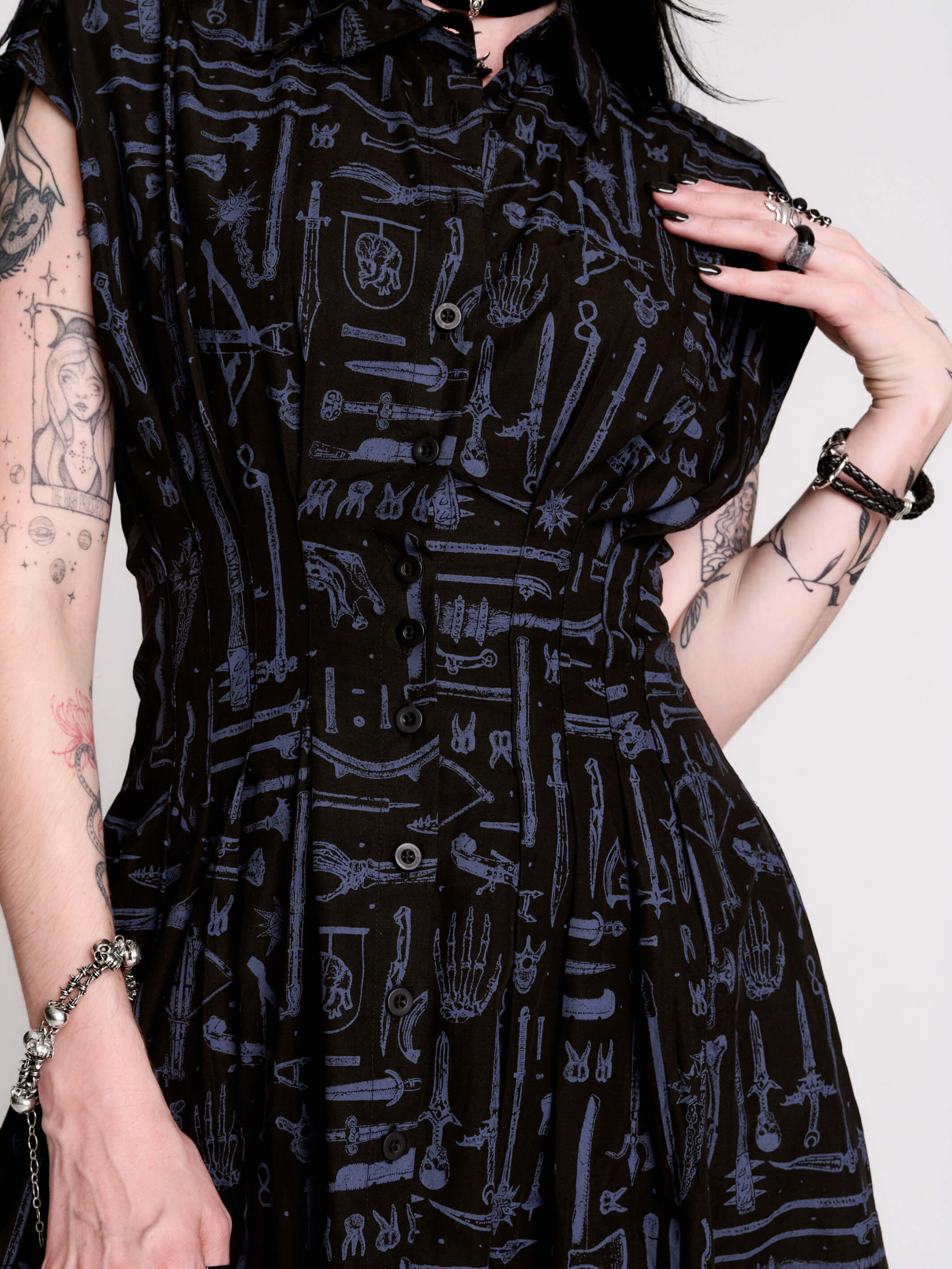 a button-front shirt dress featuring a striking medieval-inspired print with weaponry and macabre motifs.