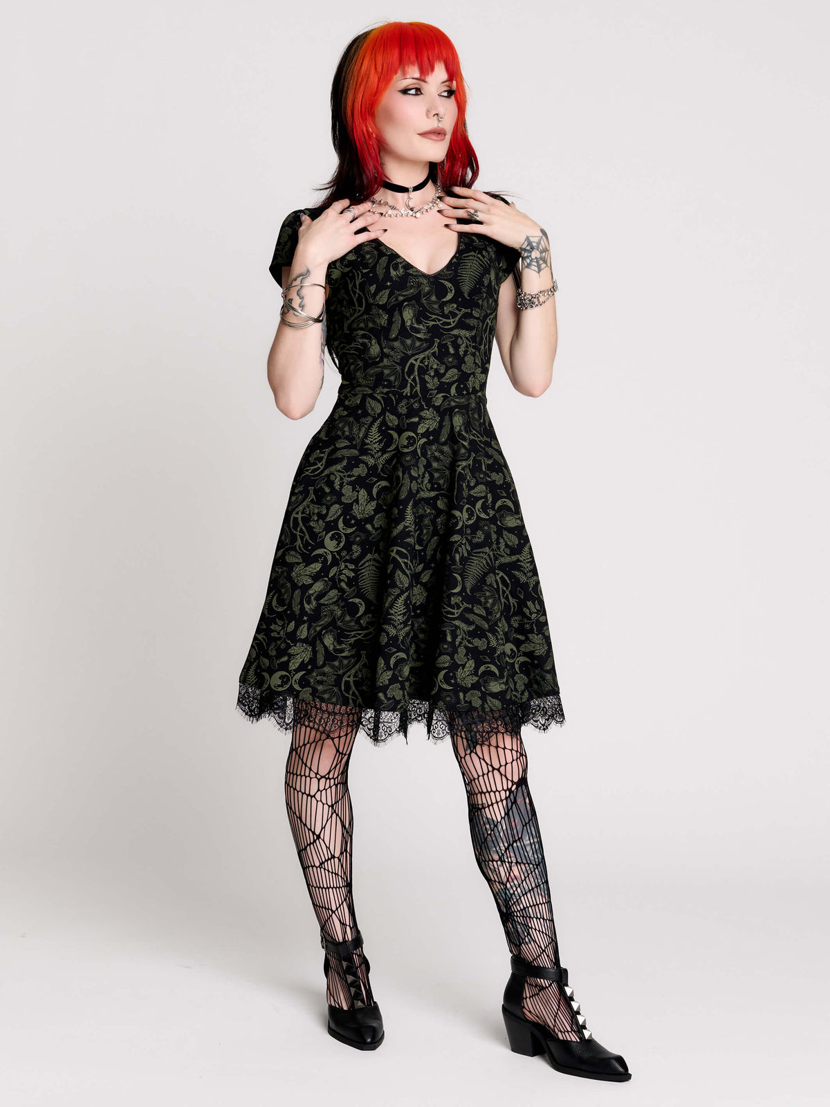 short black dress with a green leafy lace pattern, featuring cap sleeves, a V-neckline, side pockets, and a scalloped lace hem.