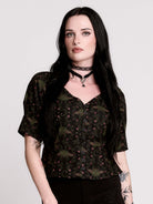 A short-sleeve button-up blouse featuring a dark green and black gothic pattern with pink accents.