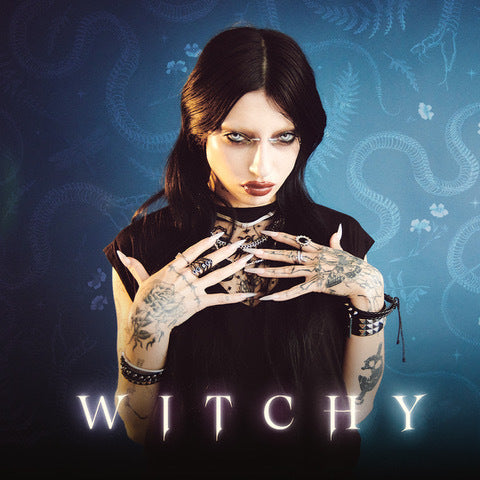 Woman with tattoos holding her hands in front of a mystical background with 'WITCHY' text.