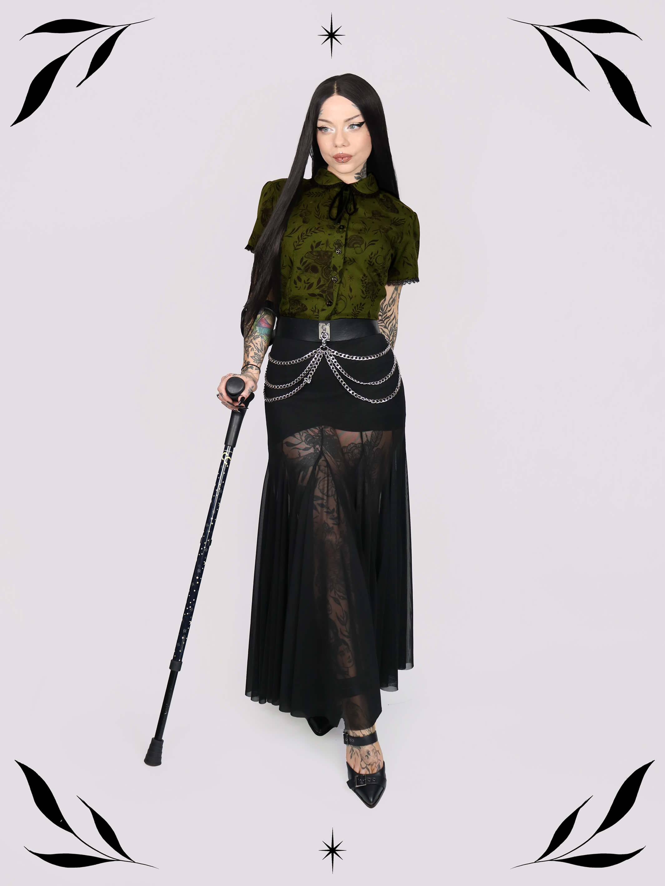 a short-sleeve olive green blouse with a dark botanical pattern, black lace trim collar with black ribbon tiedetail and black buttons. 
