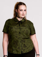 a short-sleeve olive green blouse with a dark botanical pattern, black lace trim collar with black ribbon tiedetail and black buttons. 