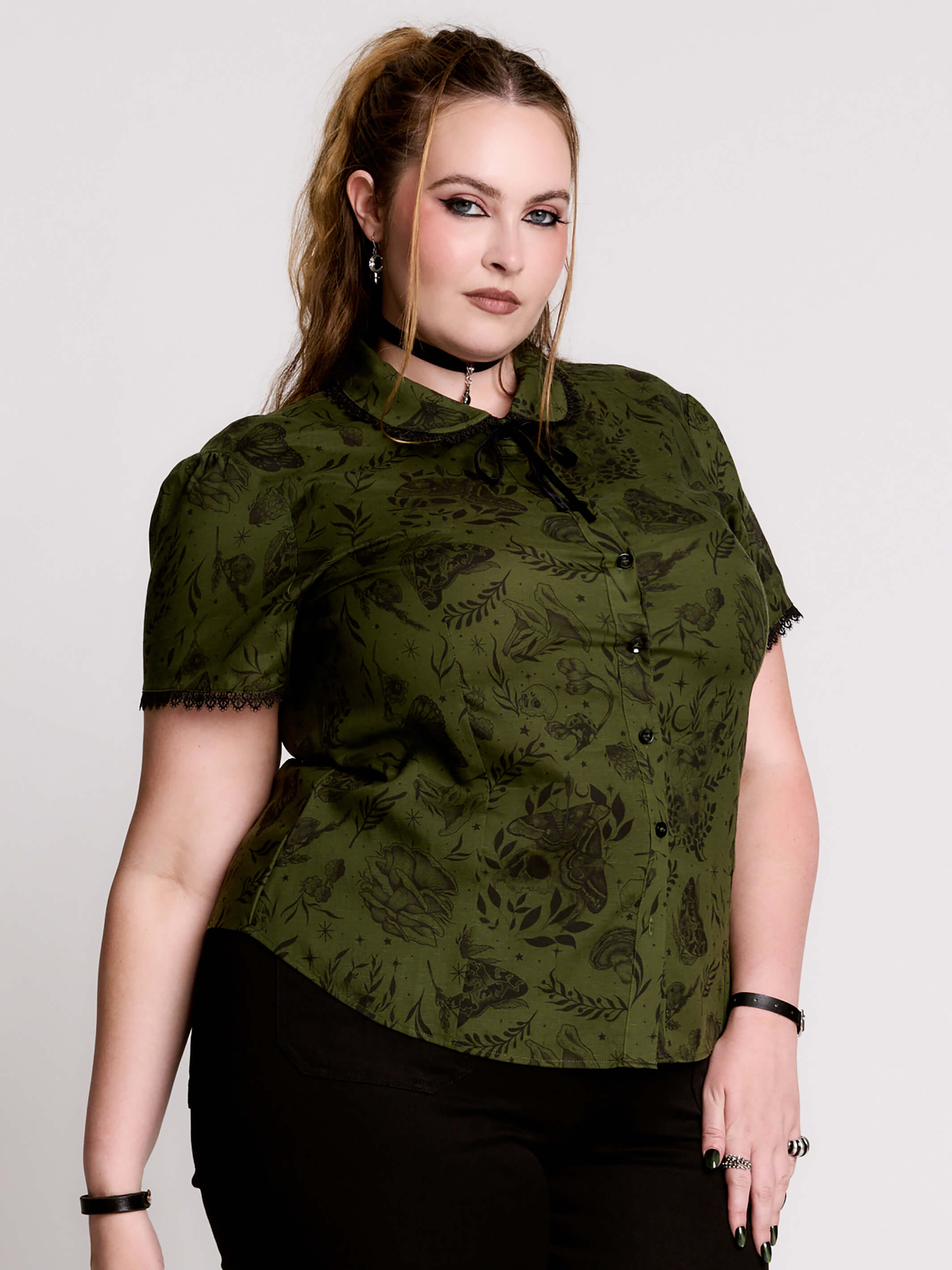 a short-sleeve olive green blouse with a dark botanical pattern, black lace trim collar with black ribbon tiedetail and black buttons. 